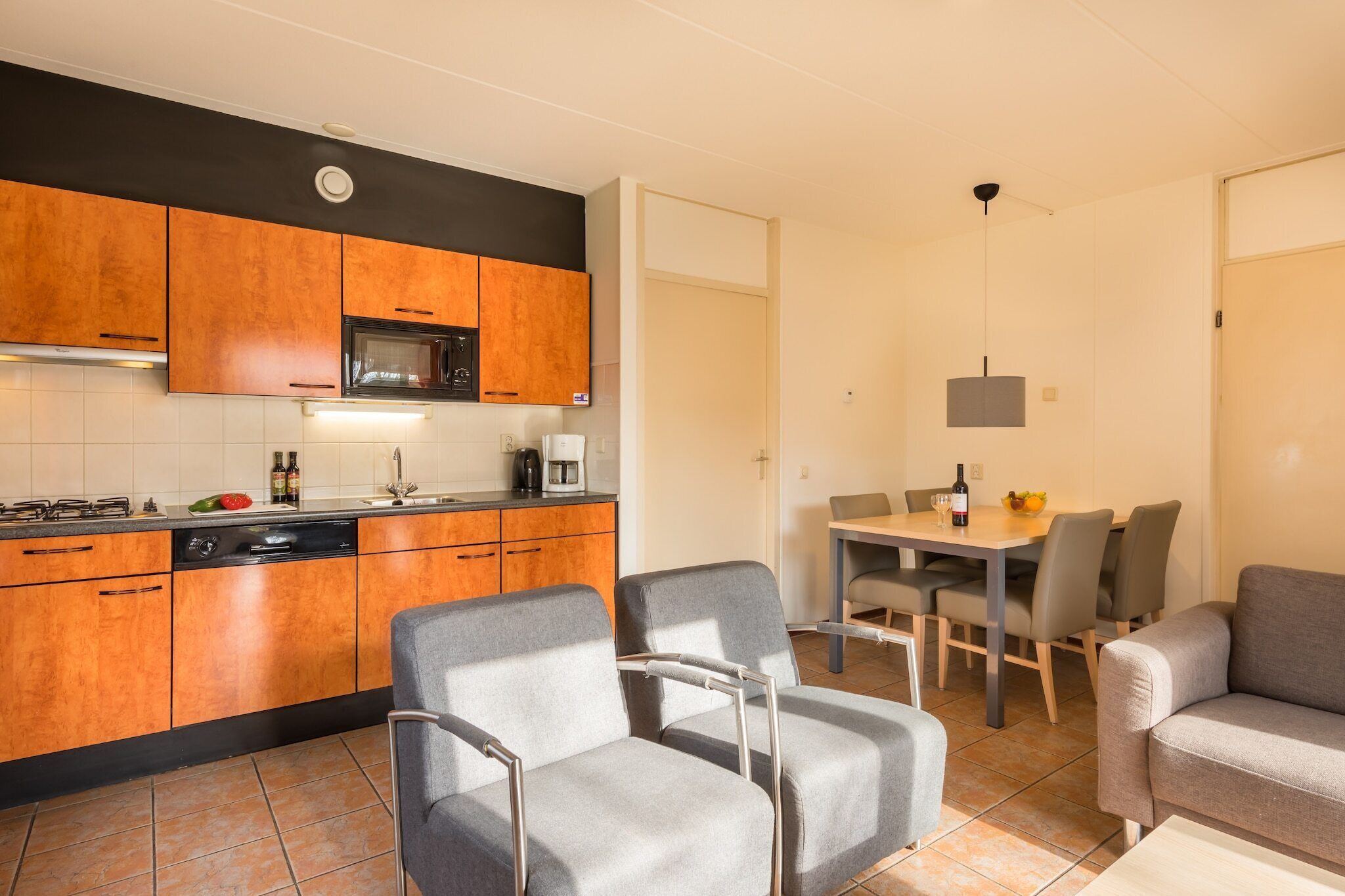 A modern kitchen with wooden cabinets, a microwave, and a dining area with grey chairs and a table.