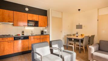 A modern kitchen with wooden cabinets, a microwave, and a dining area with grey chairs and a table.