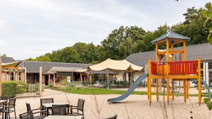 A playground with a slide and a climbing structure, surrounded by outdoor seating and covered areas. - Forest Stay with Shared Pool (Borger)