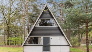 A small, modern, triangular-shaped building with a dark roof and white walls, surrounded by trees.