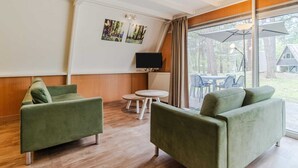 A room with two green sofas, a TV, a small table, and a large window with curtains.
