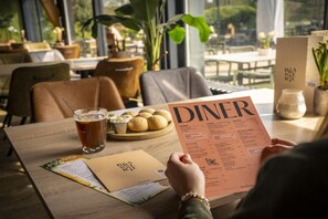 Iemand houdt een menukaart vast aan een restauranttafel, met een drankje en een bord eten.