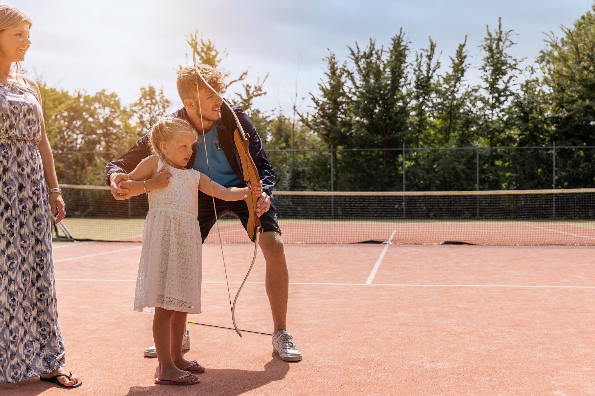 A tennis court with a net, a fence, and trees in the background.