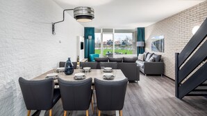 Un salon moderne avec un coin repas, agrémenté d’un mur en briques, d’un escalier et offrant une vue sur l’extérieur.