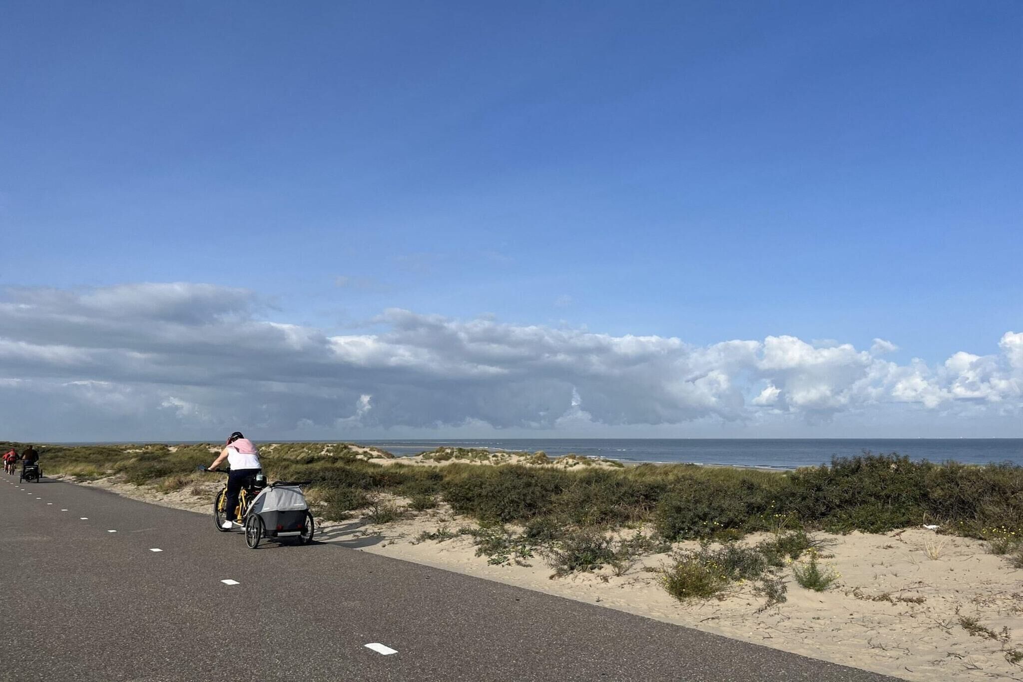 Un chemin pavé longe une plage bordée de dunes, sous un ciel dégagé.