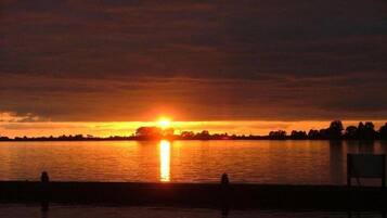 A sunset over a calm body of water with silhouettes of trees and a chair in the foreground.
