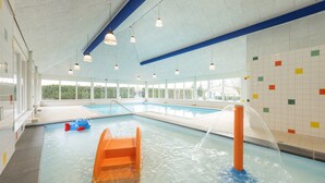 An indoor swimming pool with clear water, a blue and orange slide, and a water fountain. - Bungalow in Veluwe with Infrared Sauna (Putten)