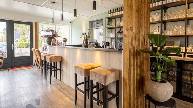 A bar area with wooden stools, a bar counter, and shelves stocked with bottles and glasses.