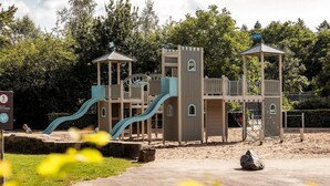 A playground with a slide, climbing structures, and a fenced area. - Designer Chalet in the Veluwe (Wissel/Epe)