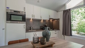 A modern kitchen with white cabinets, a built-in oven, a large vase, and a coffee maker. - Designer Chalet in the Veluwe (Wissel/Epe)