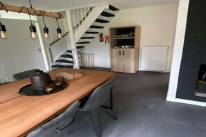 A dining area with a wooden table, chairs, and hanging light fixtures. A staircase with a black and white pattern leads to another room. - Holiday Home near Biesbosch & Breda (Oosterhout)