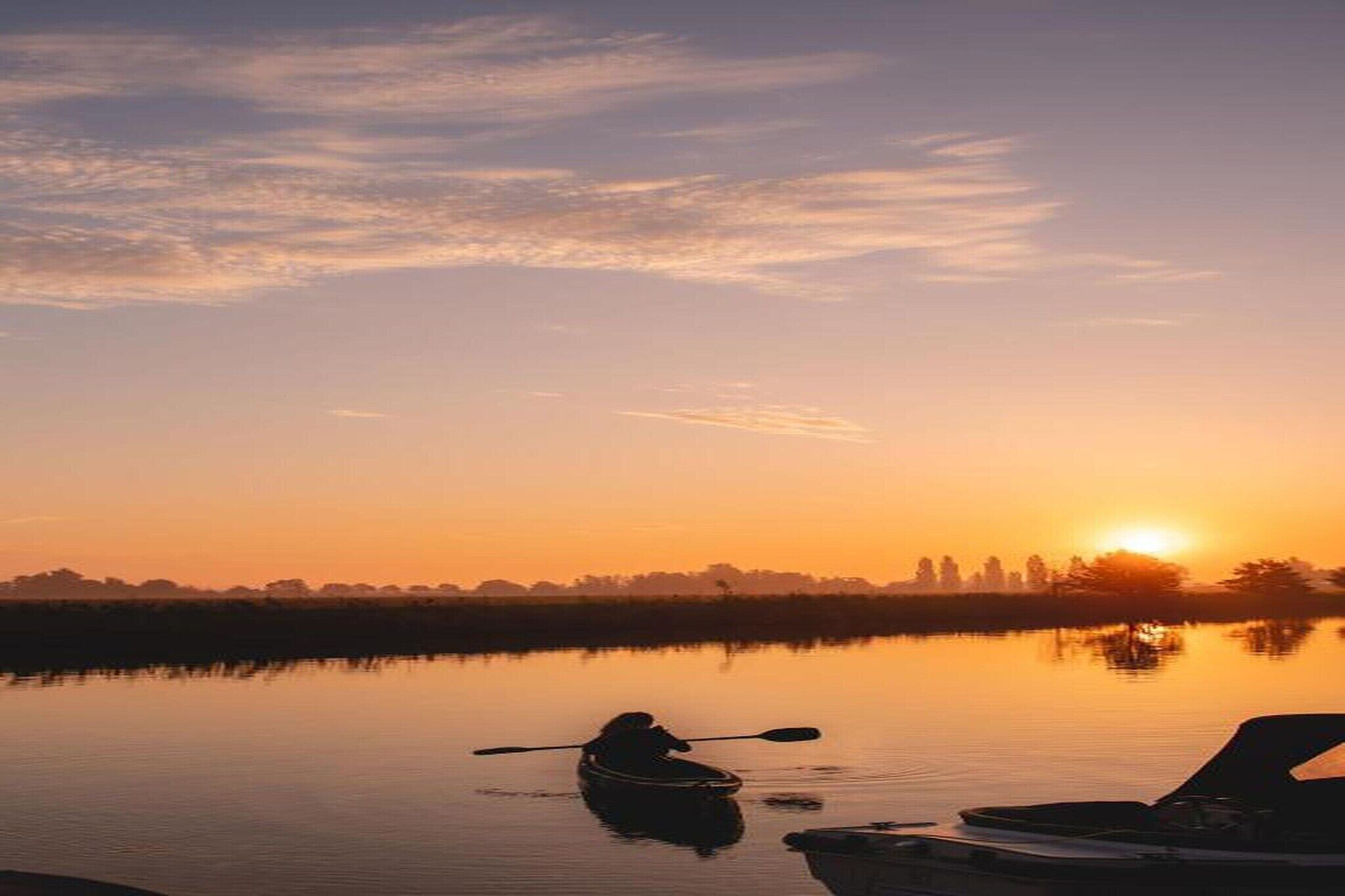A serene sunset over a calm lake with a kayak and a boat docked nearby.