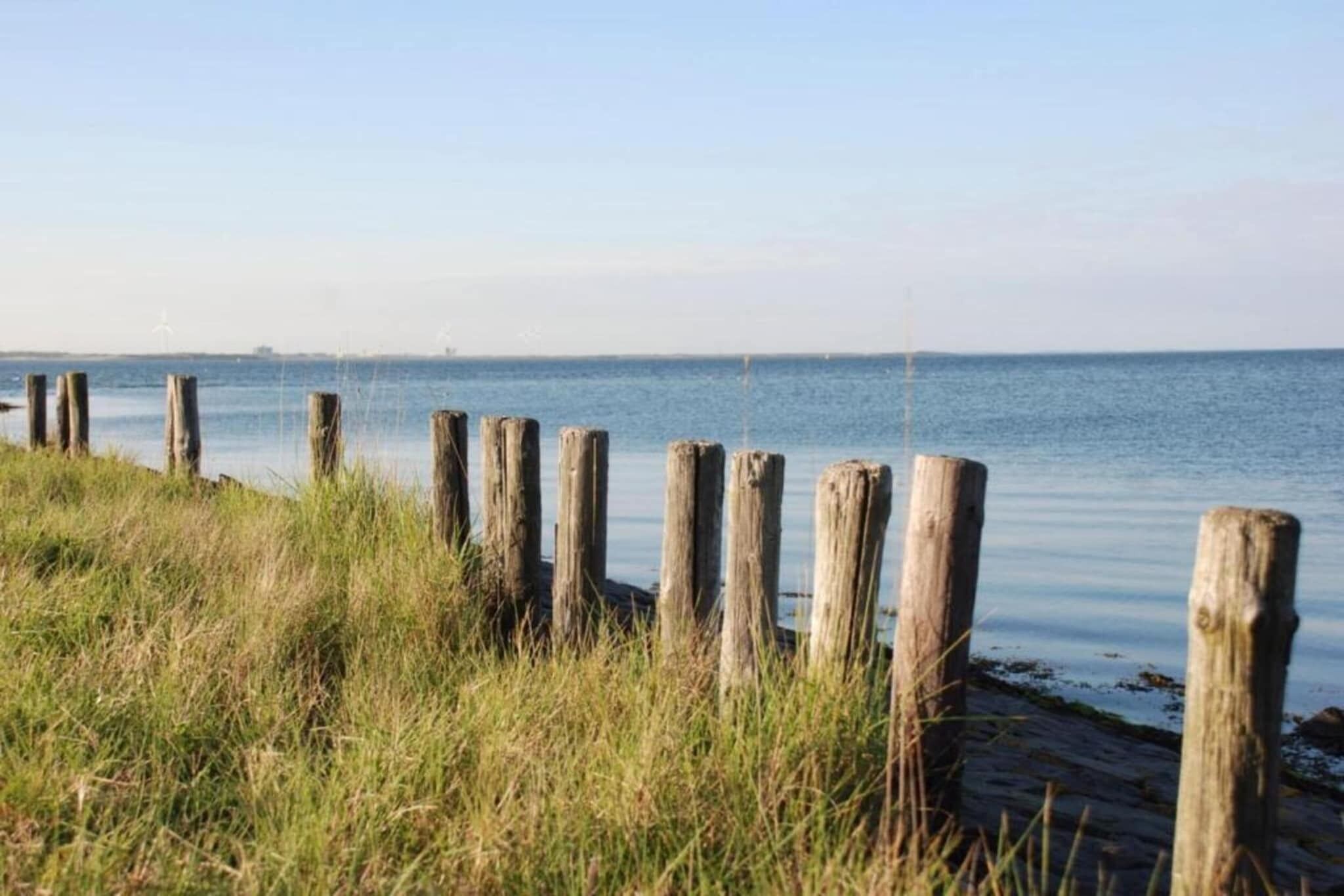 A coastal scene with wooden posts and grass in the foreground, leading to calm water.
