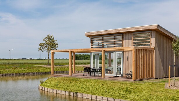 A modern house with a wooden exterior, large glass windows, and a patio area with outdoor furniture.