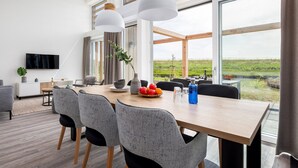 A modern dining area with a wooden table, grey upholstered chairs, and a large window offering a view of a grassy field.