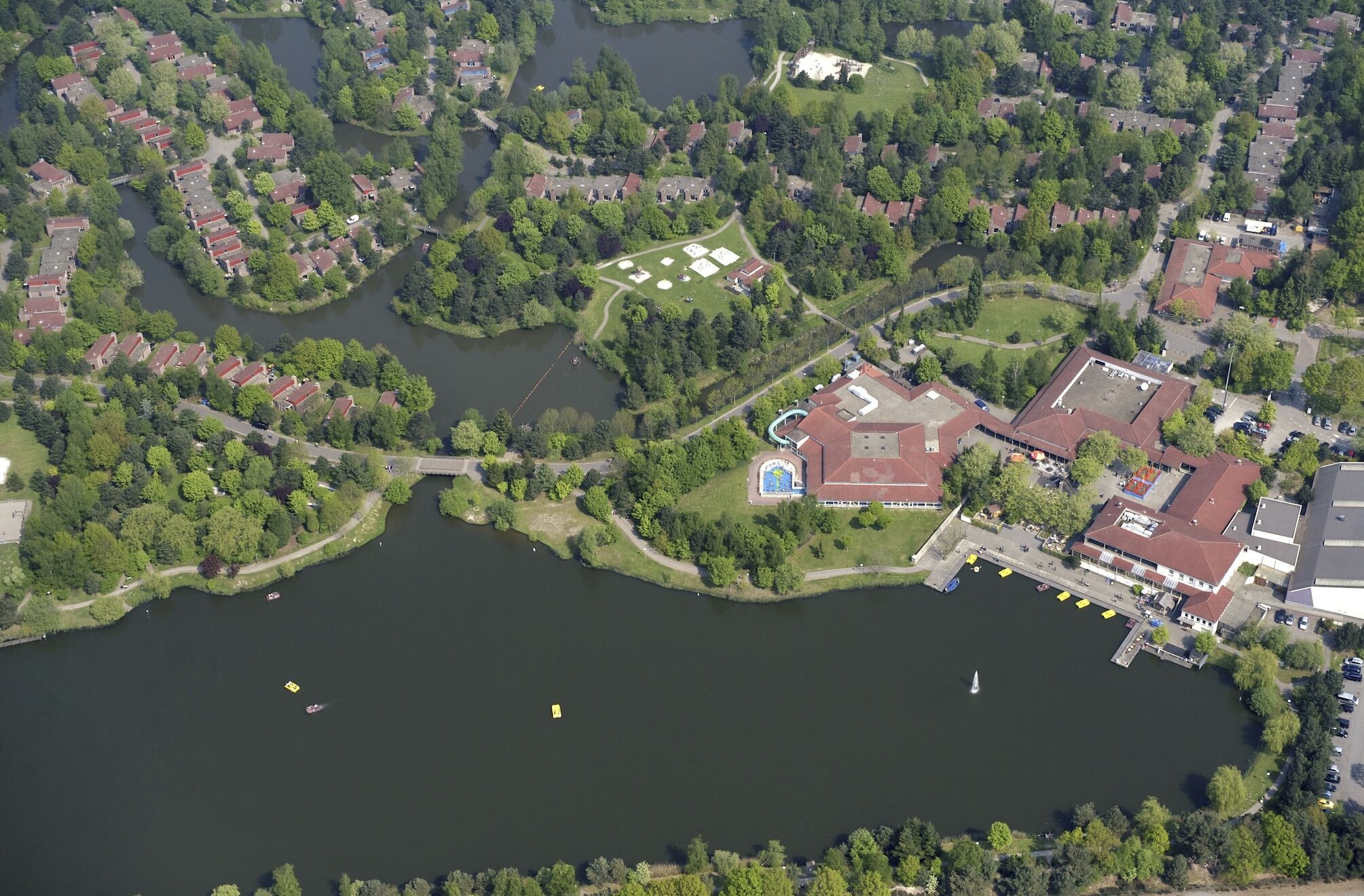 Vue aérienne d’un quartier résidentiel avec des maisons, un lac et un complexe sportif.
