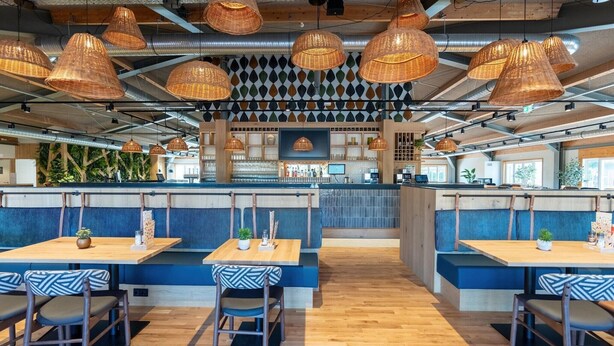 A modern restaurant with wooden tables and blue cushioned booths, featuring woven pendant lights and a patterned wall. - Sauna Stay by Moselle River (Cochem)