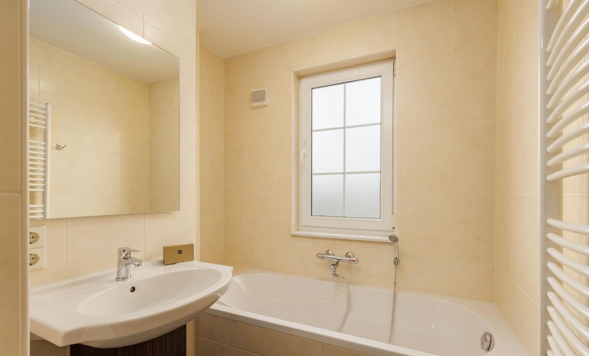 A bathroom with a sink, mirror, window, and bathtub.