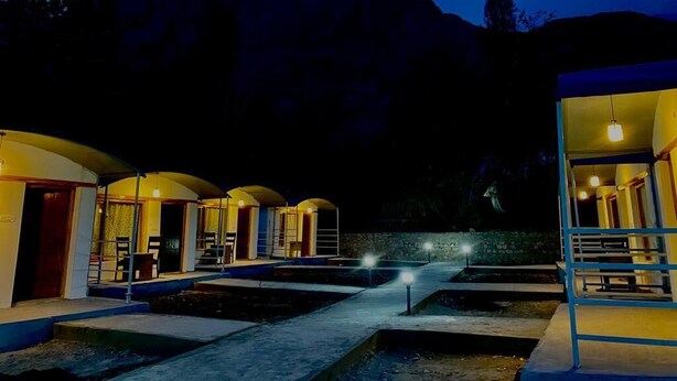 A series of connected buildings with arched roofs, a central pathway, and a mountainous backdrop.