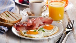 A breakfast setting with toast, eggs, bacon, coffee, and orange juice on a wooden table.