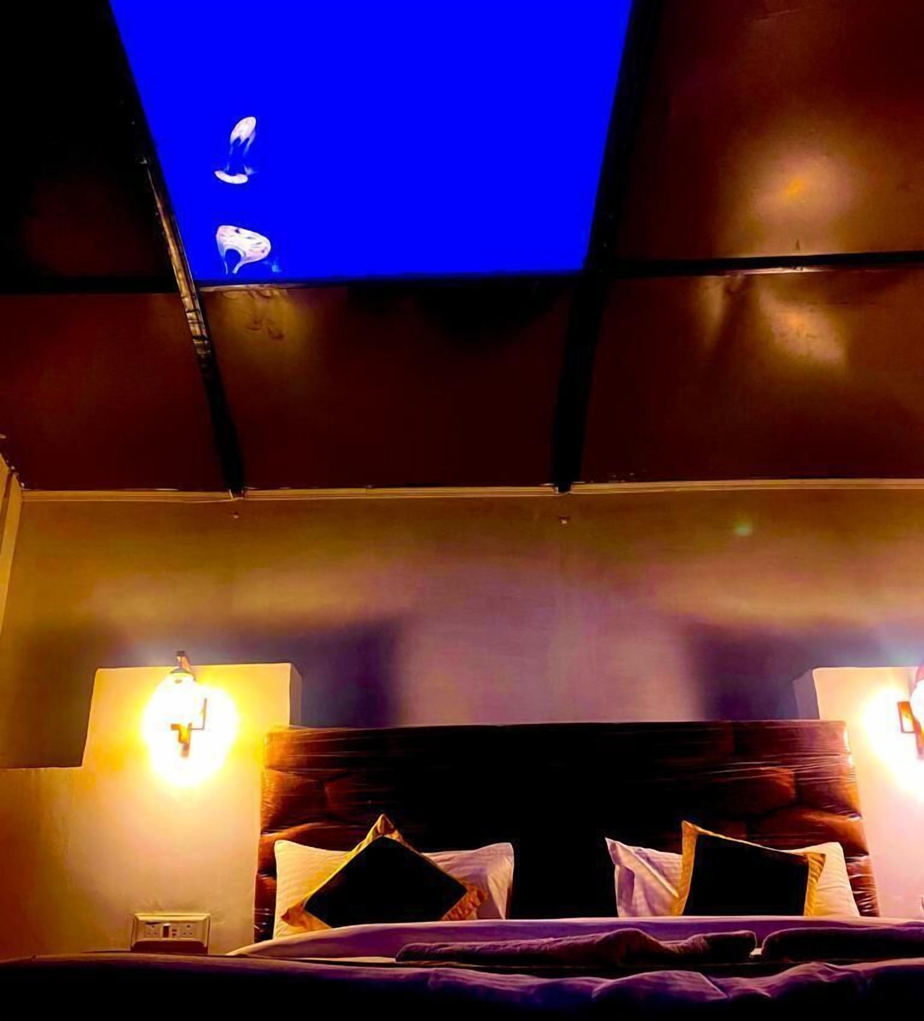 A bedroom with a dark headboard, two bedside lamps, and a bed with pillows.