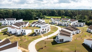 A residential area with modern white houses arranged in a curved layout, surrounded by green lawns and trees.