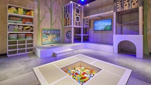 A play area with a playhouse, shelves with toys, a television screen, and a play mat.