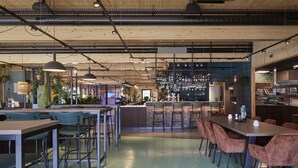 A modern bar area with wooden ceiling, bar stools, and a counter with a variety of bottles and glasses.