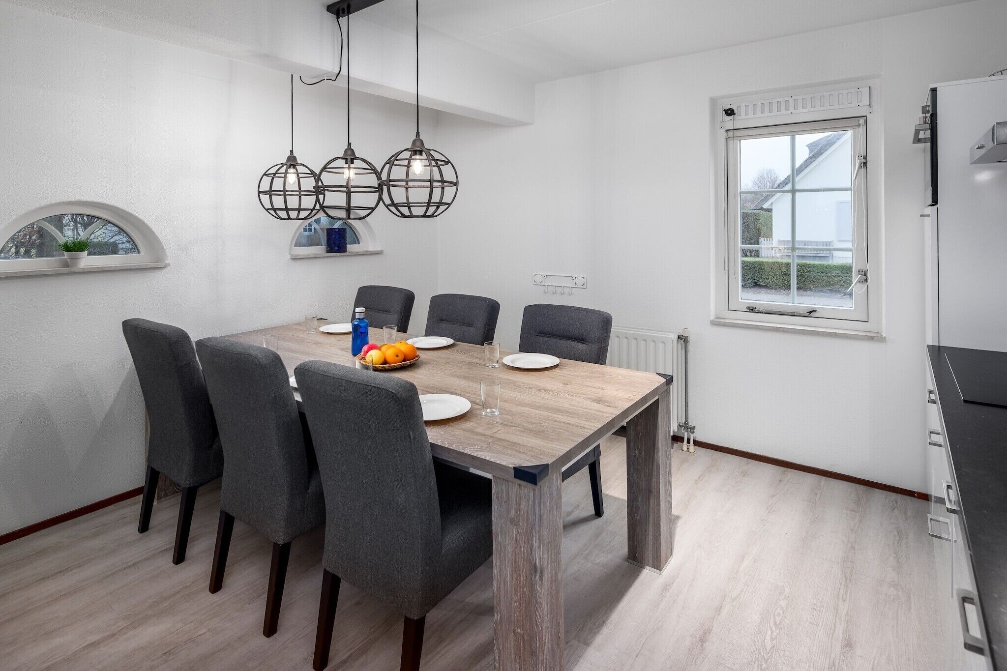 Un comedor moderno con una mesa de madera, sillas tapizadas en gris e iluminación colgante.