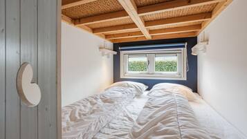A narrow room with a single bed, a window with a view of greenery, and a wooden ceiling.