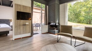 A modern living room with a fireplace, a sofa, a TV mounted on the wall, and a view of the outdoors.
