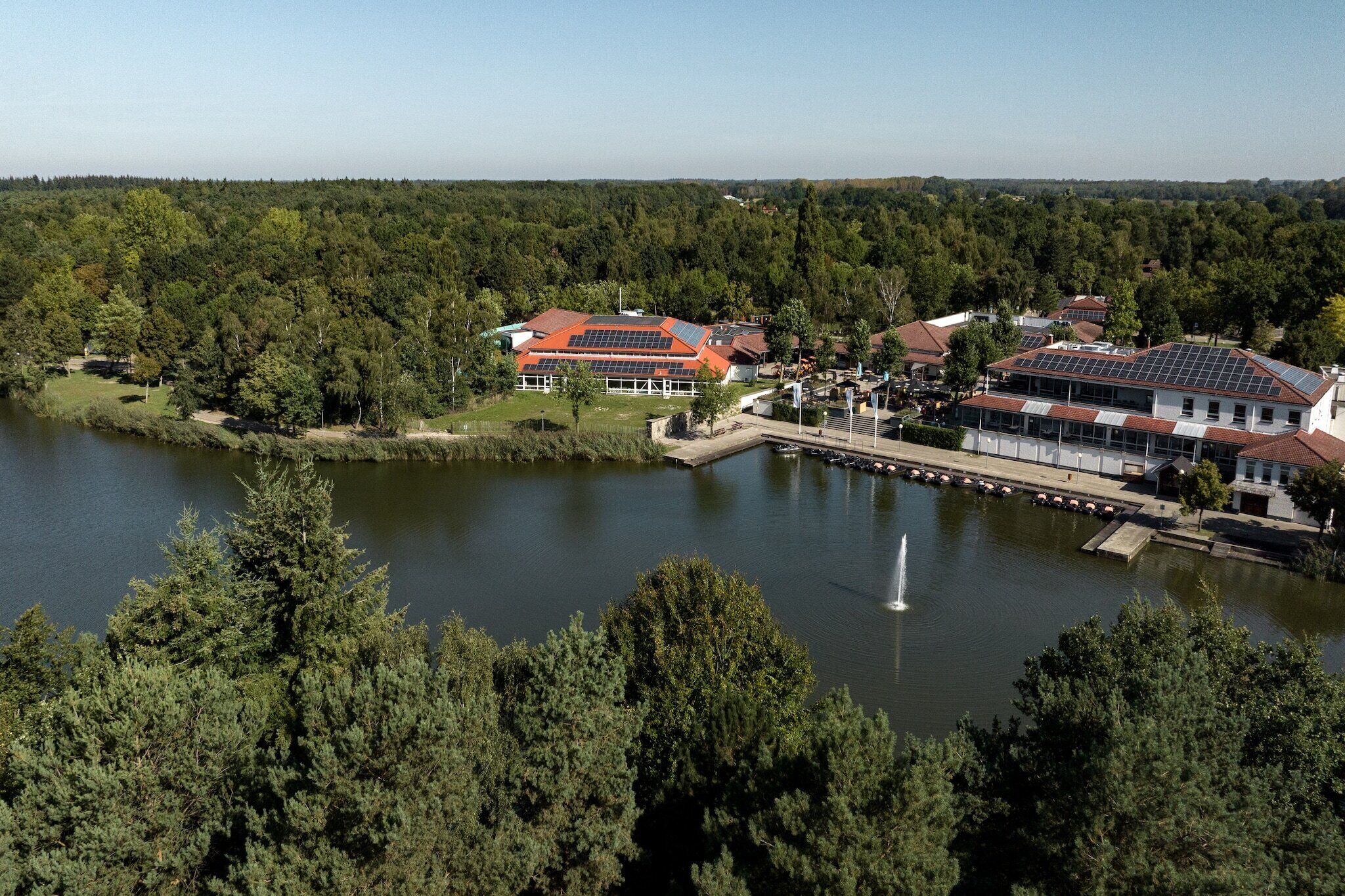 A lakeside property with buildings featuring solar panels, a dock, and a fountain.