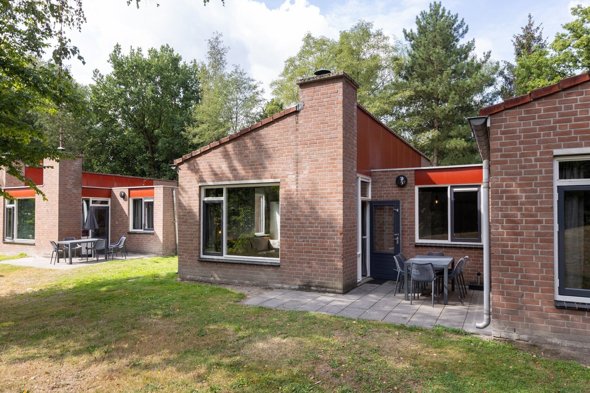 Ein Backsteinhaus mit großen Fenstern und einer Terrasse mit Außenbestuhlung.