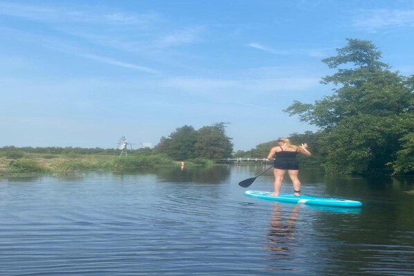 A person paddleboarding on a calm river with trees and a bridge in the background.