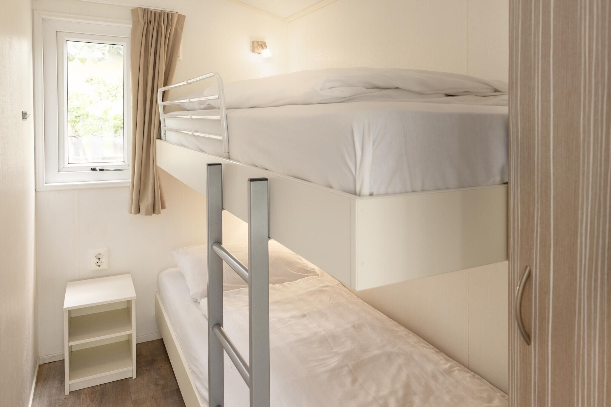 A bunk bed room with a window, a small white nightstand, and a wooden wardrobe.