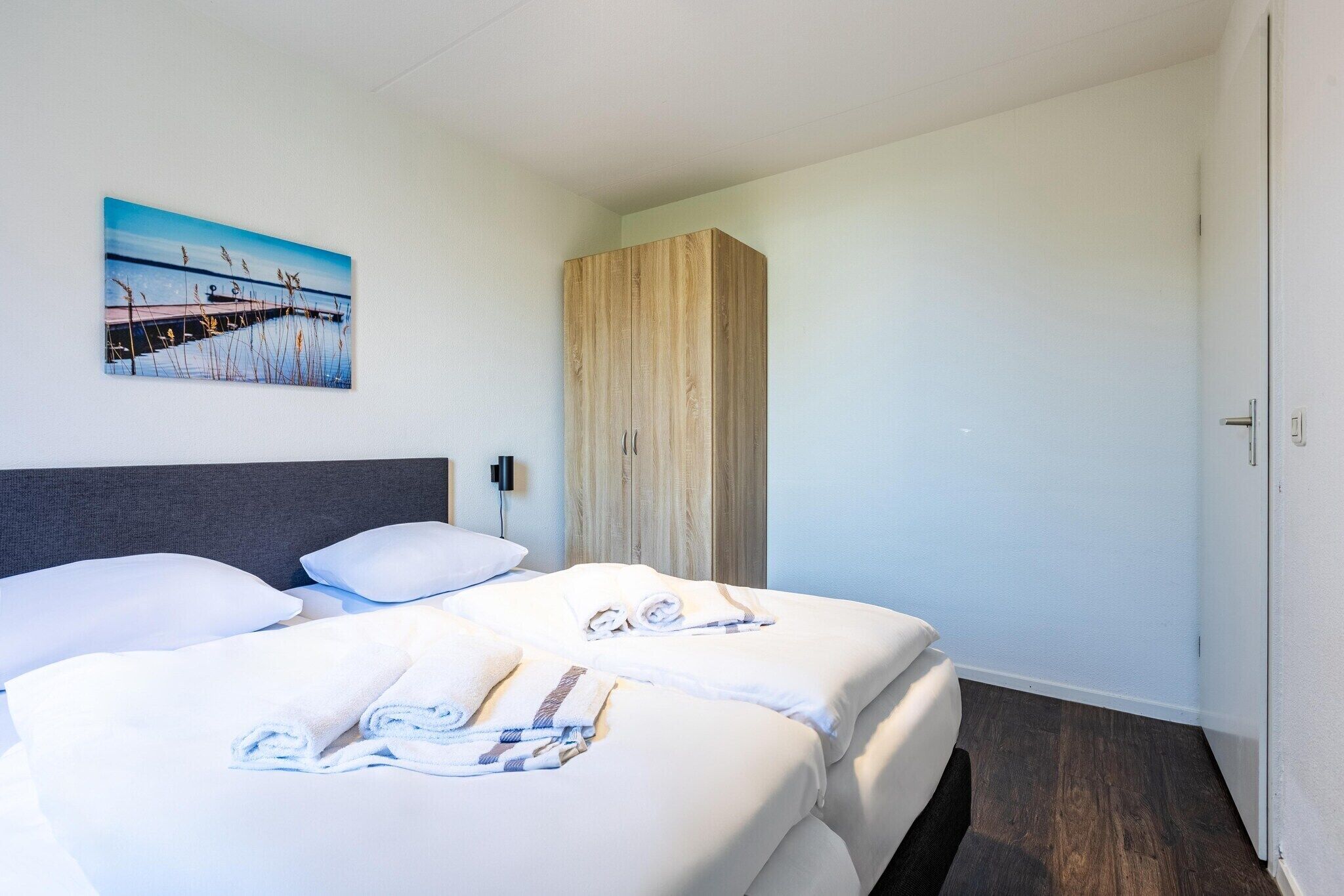 Ein Hotelzimmer mit zwei Betten, einem Holzschrank, einem Bild an der Wand und einer Tür rechts.