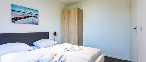 Ein Hotelzimmer mit zwei Betten, einem Holzschrank, einem Bild an der Wand und einer Tür rechts.