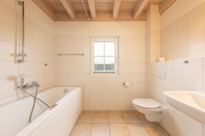 A bathroom with a bathtub, toilet, and a window.