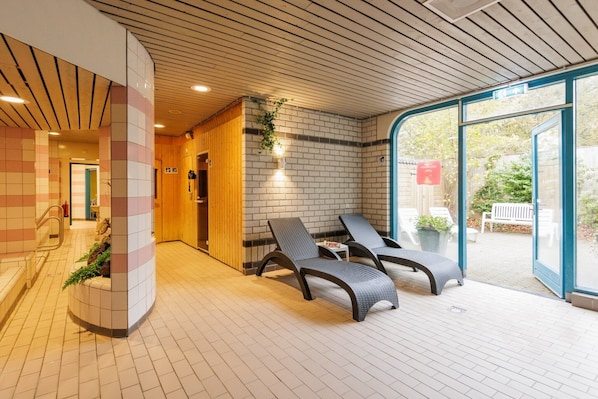 A modern indoor relaxation area with lounge chairs, a brick wall, and a glass door leading outside. - Wellness Stay with Sauna (Borger)