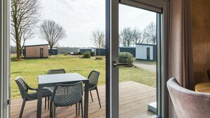 A patio with a table and chairs, a wooden deck, and a view of a residential area with houses and trees. - Wellness Stay with Sauna (Borger)