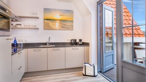 Een moderne keuken met een groot raam, een schilderij van een zonsondergang en uitzicht op een gebouw met rode daken.
