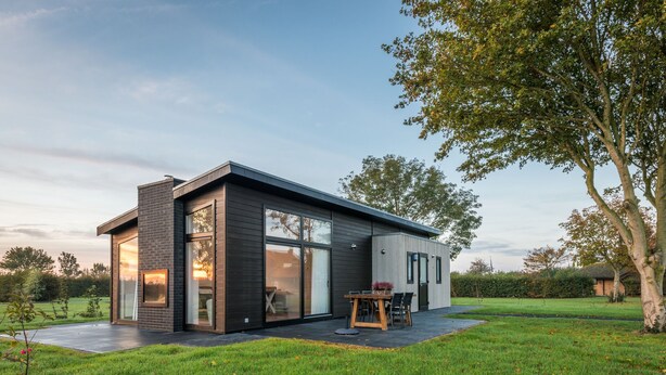 Une maison moderne dotée d’une grande porte vitrée, d’un patio avec une table et des chaises, et d’une pelouse bien entretenue.