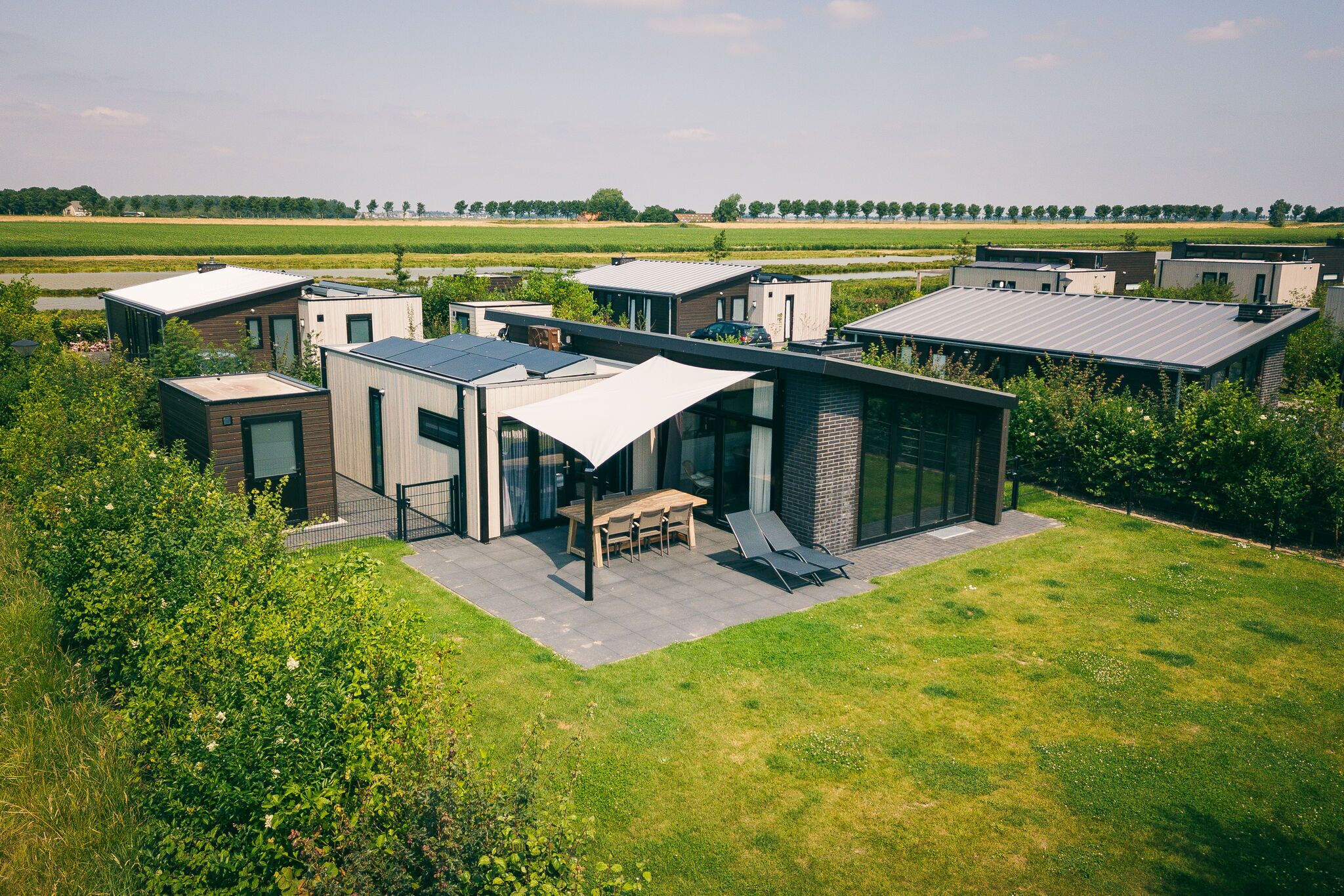 A modern house with a patio, a dining area, and a view of a green field.