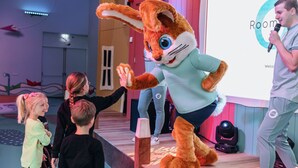 Een persoon in een konijnenkostuum op een podium met een microfoon, die met kinderen in contact staat.