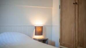 A neatly made bed with a bedside lamp, a wooden wardrobe, and a white wall. - Holiday Home near Breda & De Biesbosch Park (Oosterhout)