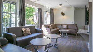 A modern living room with two sofas, two round tables, and large windows with curtains. - Holiday Home near Breda & De Biesbosch Park (Oosterhout)