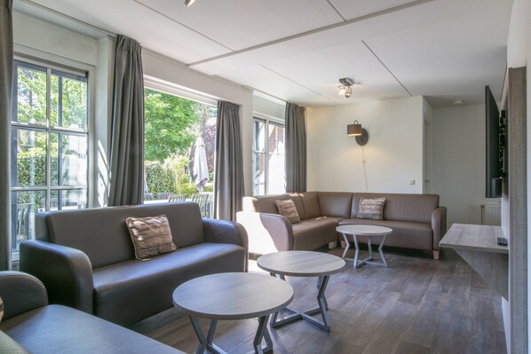 A modern living room with two sofas, two round tables, and large windows with curtains.