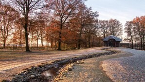 A gravel path leading to a rustic building with a thatched roof, surrounded by trees with autumn foliage.