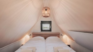 Ein gemütliches, dreieckiges Schlafzimmer mit zwei Betten, einem kleinen Fenster und einer Hängelampe.