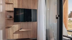 Ein modernes Wohnzimmer mit einem großen Flachbildfernseher an einer Holzwand, einem kleinen Regal mit einer Schale und einer Schiebeglastür, die zu einem Außenbereich führt.